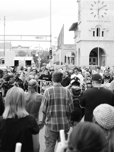 Photo: Black and white image of a group of people gathered in a circle on a street corner