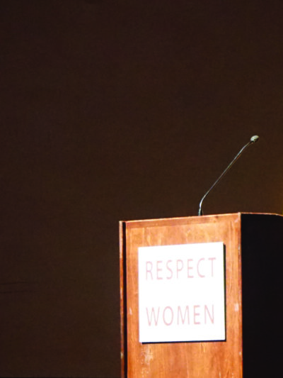 Photo: A woman stands behind a podium speaking to a crowd