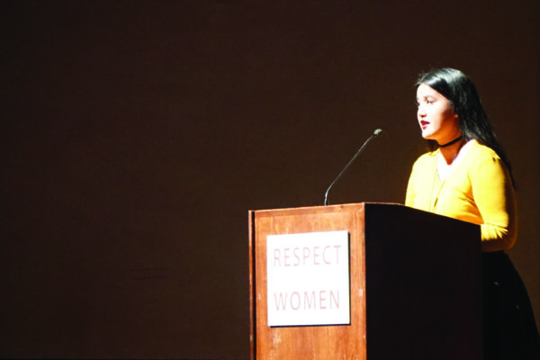 Photo: A woman stands behind a podium speaking to a crowd