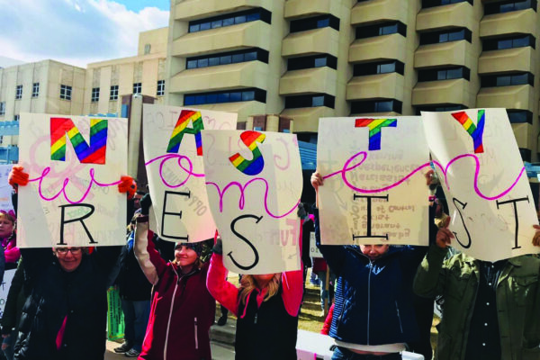 Women holding a sign that says "Women Resist"