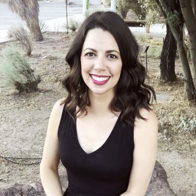 Photo: Young woman wearing a black shirt smiling at the camera in front of a colorful wall