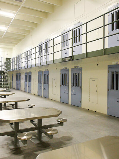 An empty cell block in a prison with tables and blue doors.