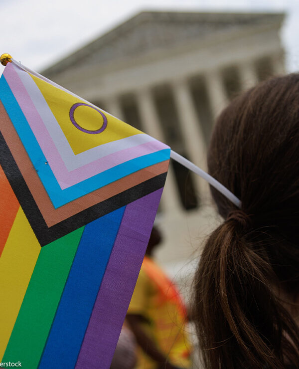 A Pride supporter (whose face cannot be seen) holds an Intersex-inclusive Pride Flag in their hair while facing the Supreme Court.