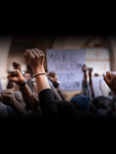 stock image of young people raising fists in the air with illegible signs of protest in the background
