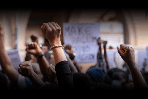 stock image of young people raising fists in the air with illegible signs of protest in the background