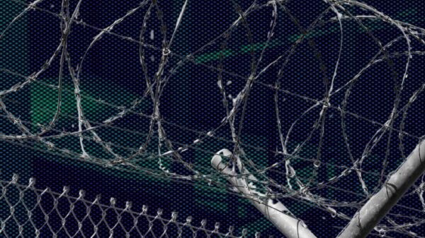 A photo of a prison fence in front of a dark and ominous view of a prison.