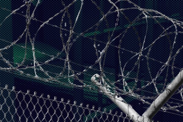 A photo of a prison fence in front of a dark and ominous view of a prison.