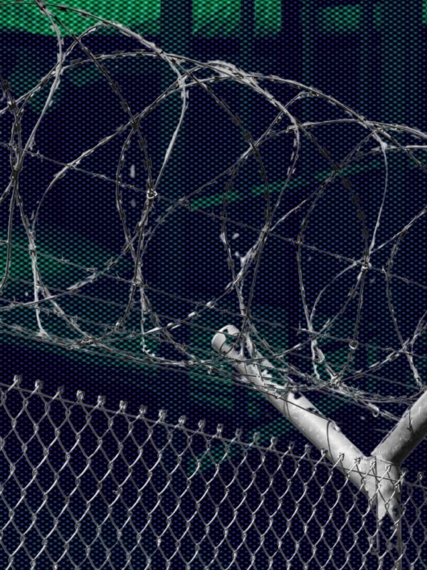 A photo of a prison fence in front of a dark and ominous view of a prison.
