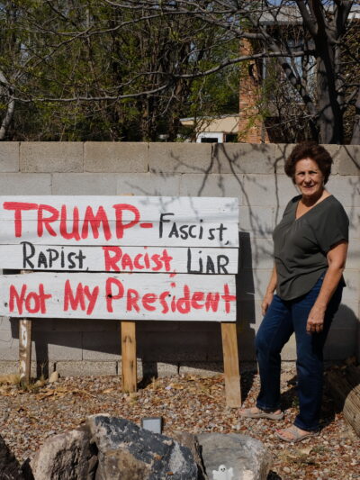A photo of Rita Padilla-Gutiérrez standing in front of her sign that reads: "Trump, racist, rapist, not my president"