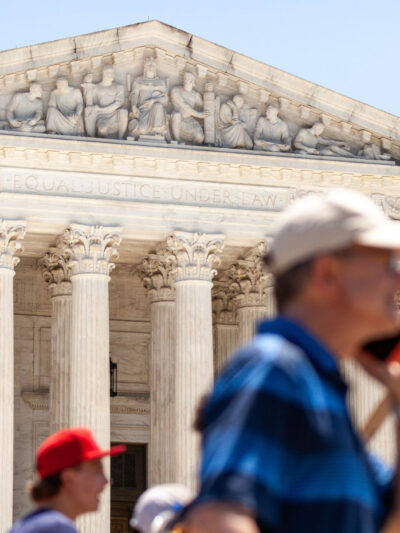 Pro-choice demonstrators (whose faces and signs are blurred) march in front of the Supreme Court and the statement on its facade, "Equal justice under law".