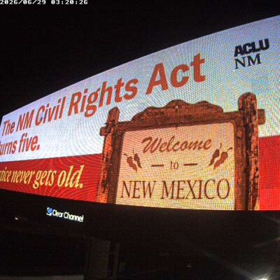 A billboard that says "The NM Civil Rights Act turns five. Justice never gets old" with a "Welcome to New Mexico" sign on it.