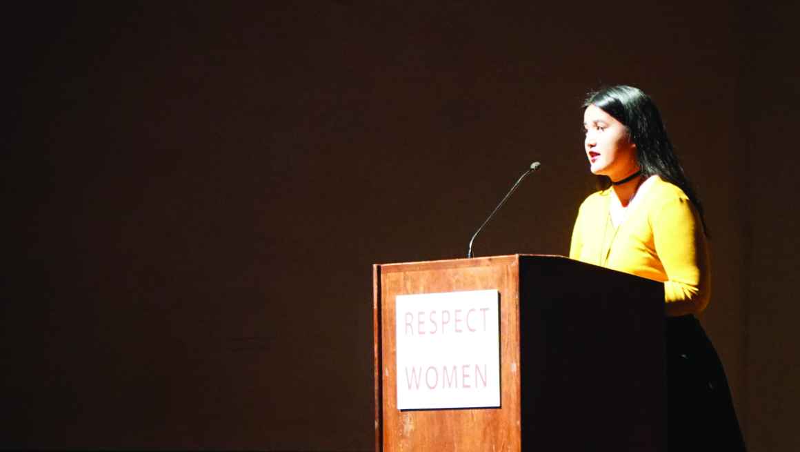 Photo: A woman stands behind a podium speaking to a crowd