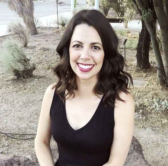 Photo: Young woman wearing a black shirt smiling at the camera in front of a colorful wall