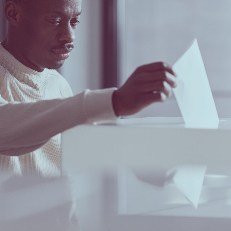 A man placing a piece of paper into a voting box.