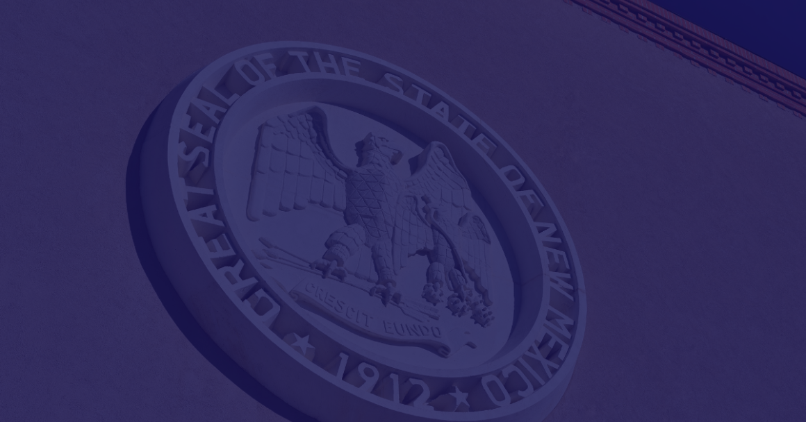 A blue tinted photo of the New Mexico State seal on the New Mexico State Capitol building.