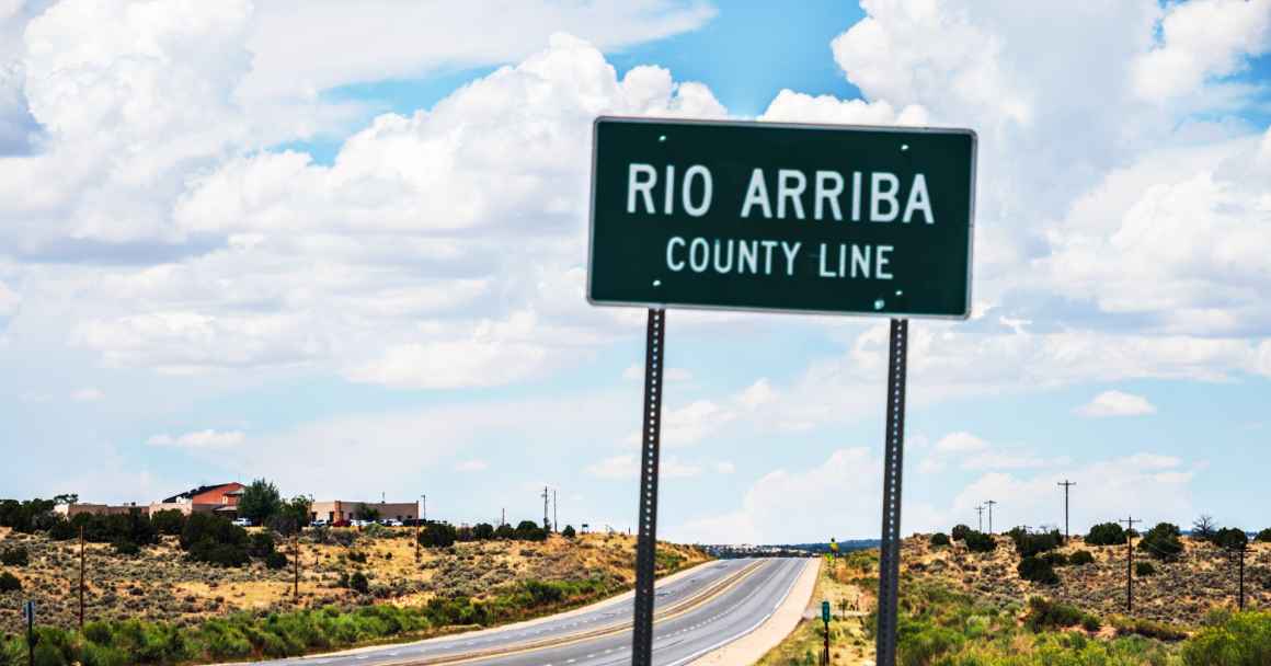 A road sign showing the Rio Arriba county line with Lybrook elementary just beyond it.