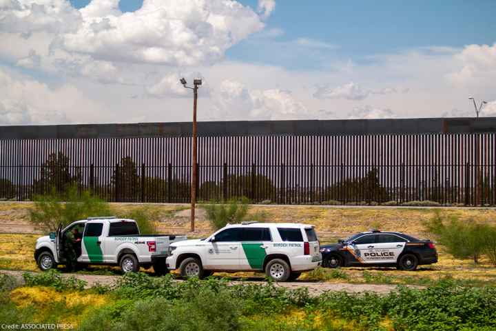 U.S. Border patrol vehicles converge with local police car by border fence.