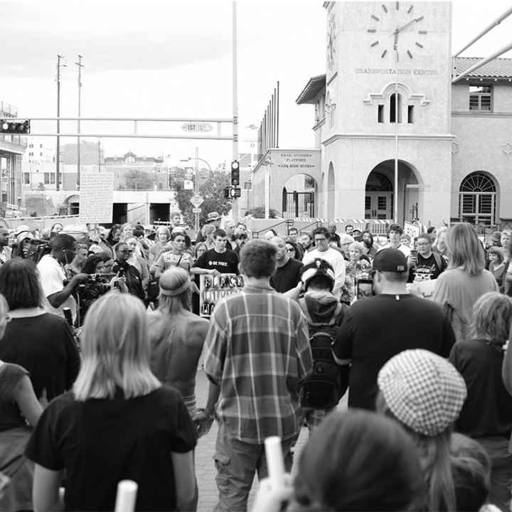 Photo: Black and white image of a group of people gathered in a circle on a street corner