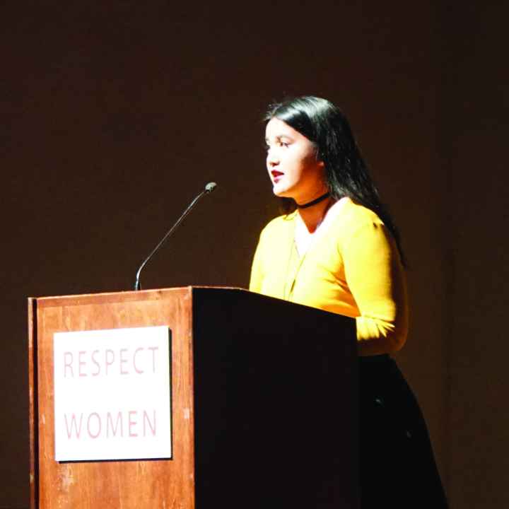 Photo: A woman stands behind a podium speaking to a crowd