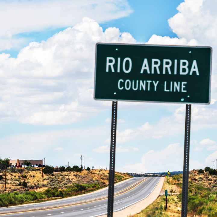 A road sign showing the Rio Arriba county line with Lybrook elementary just beyond it.