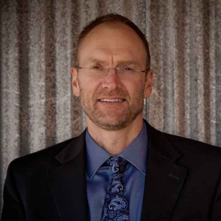 photo of a a man from the shoulders up wearing a blue shirt, tie, and black jacket